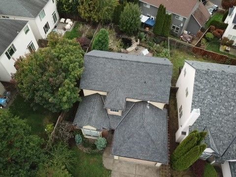 Overhead view of a house with gray roof, surrounded by trees and other homes in a neighborhood.