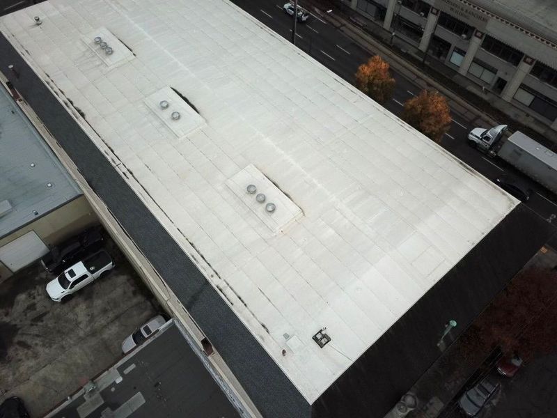 White commercial building roof with vents, surrounded by streets and buildings.