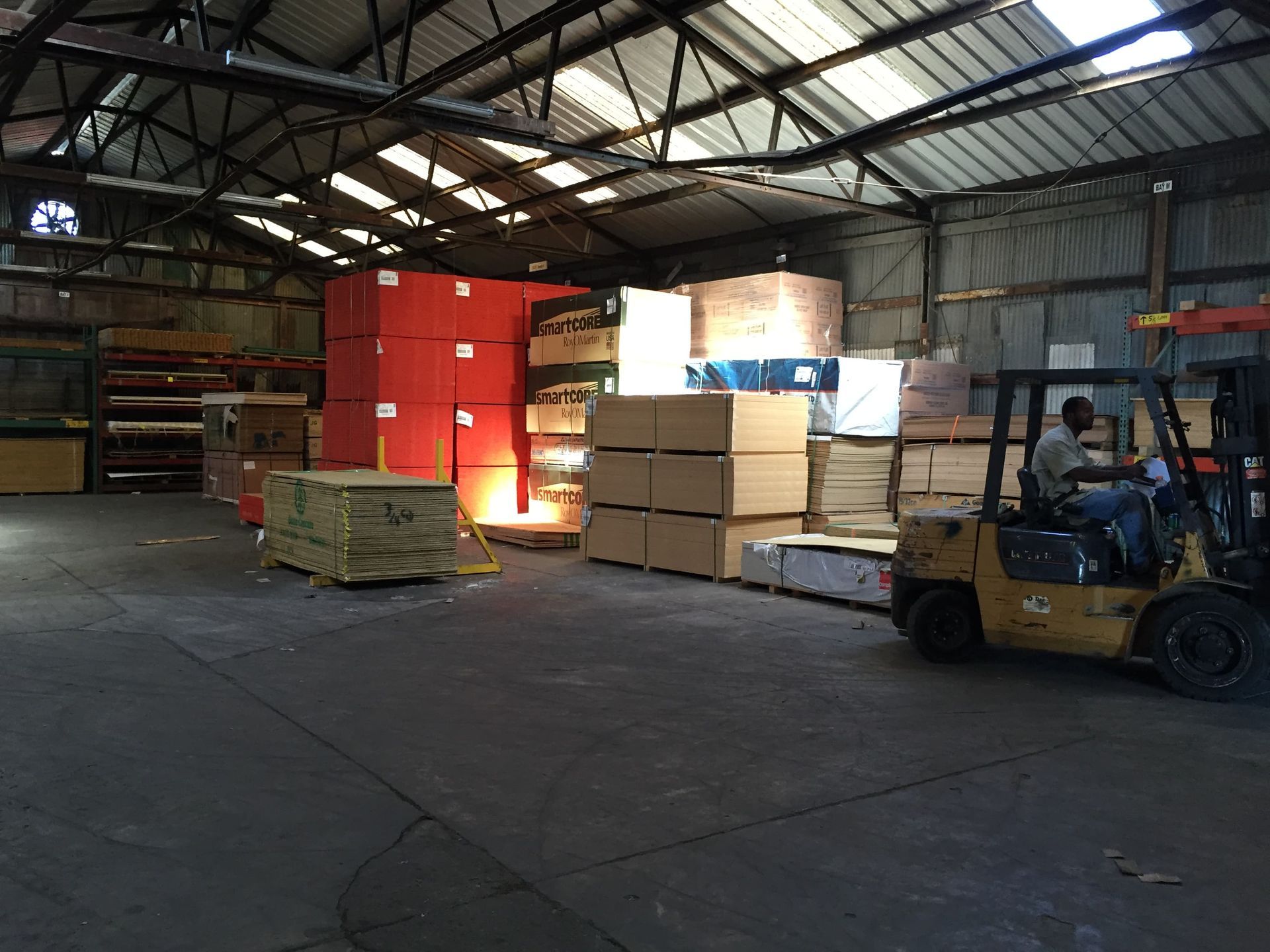 A man is driving a forklift in a warehouse filled with boxes.