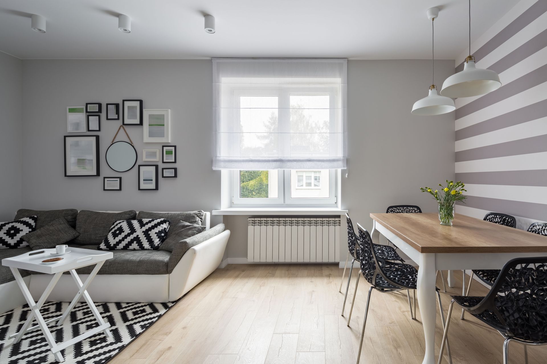 Bright modern living-dining room with gray sofa, striped rug, wooden table, and window light