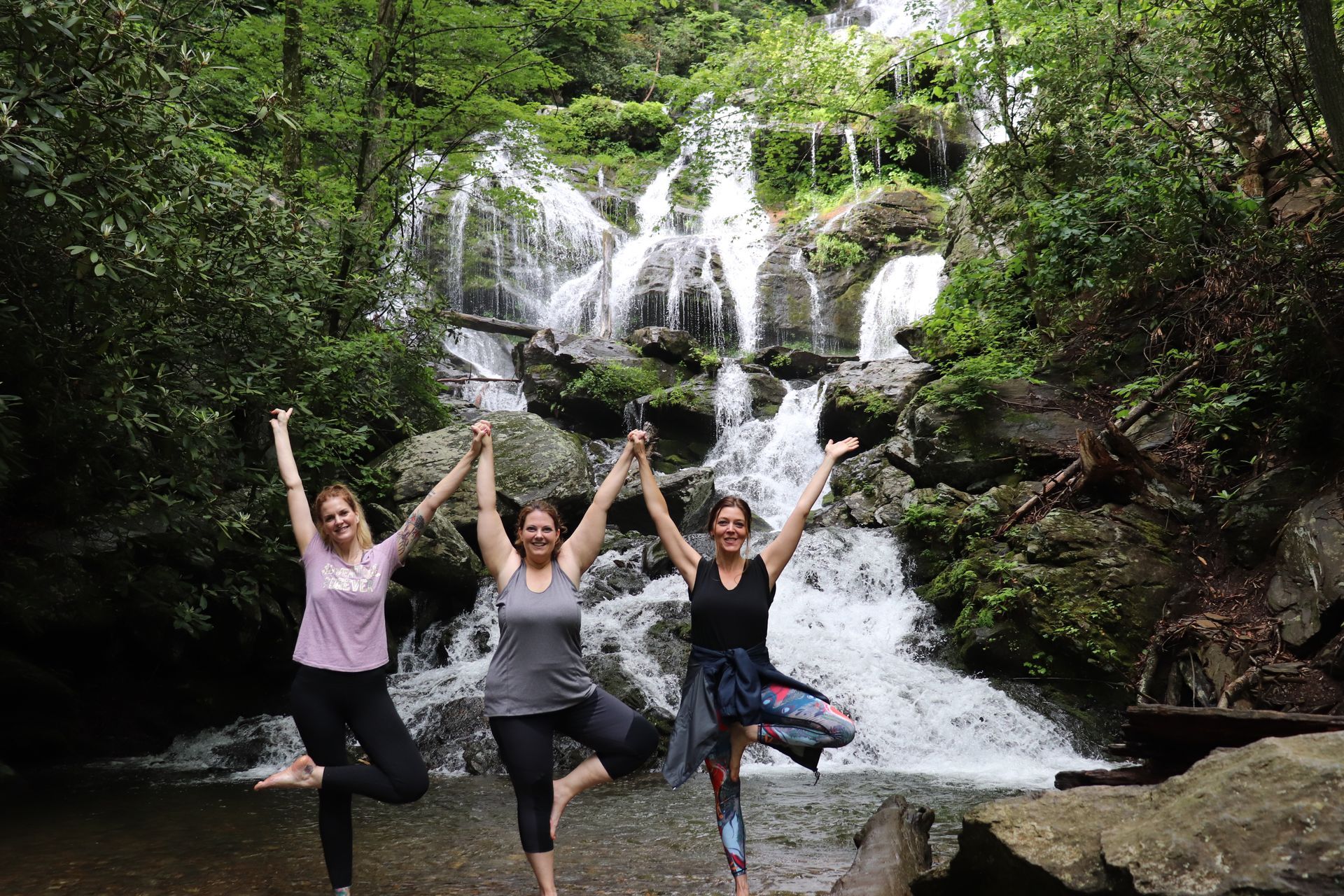 Three women are doing yoga in front of a waterfall.