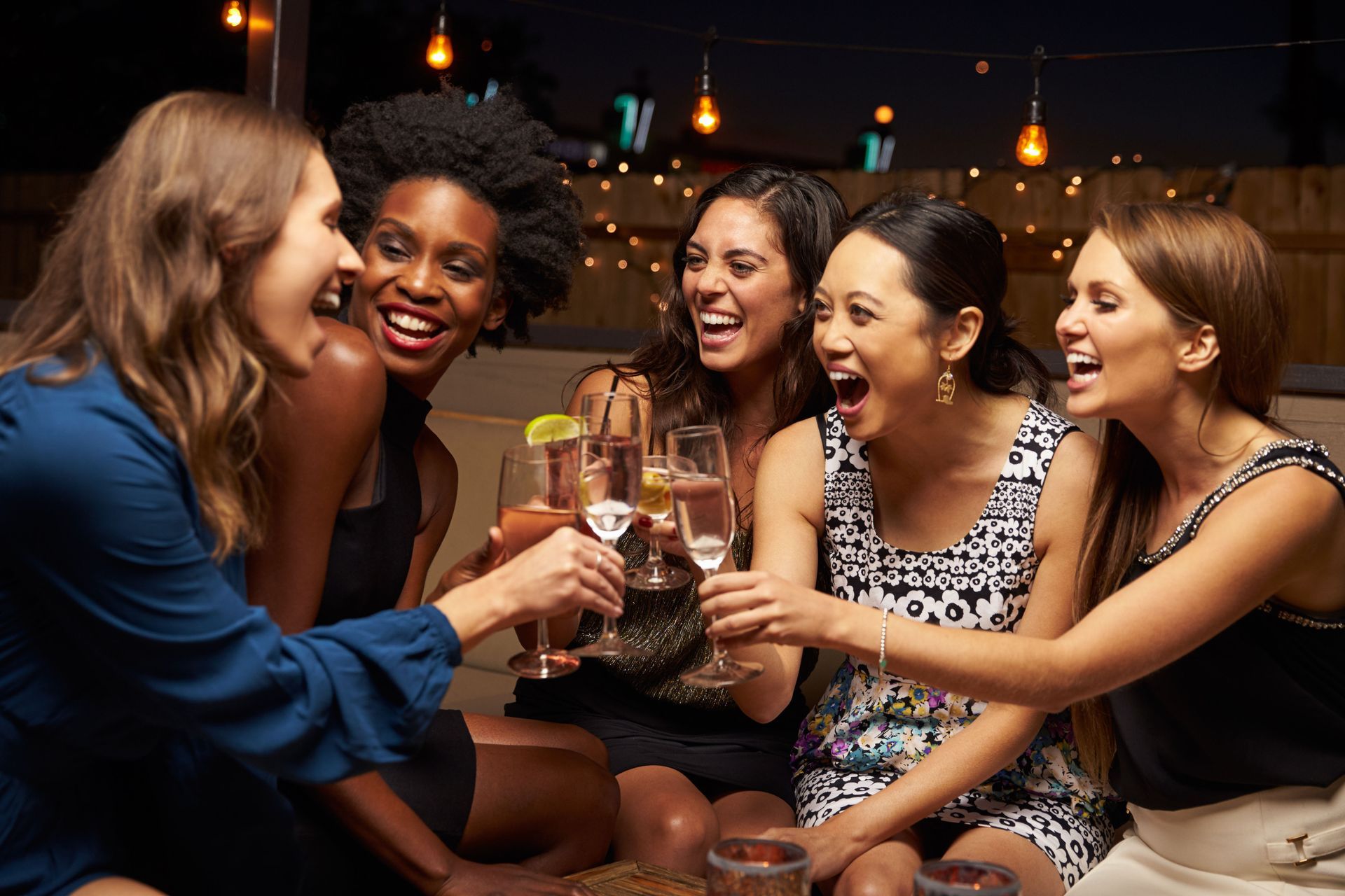 A group of women are sitting around a table drinking wine and laughing.