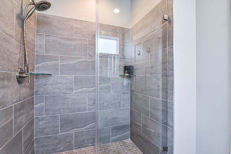 A walk in shower with a glass door and gray tiles.