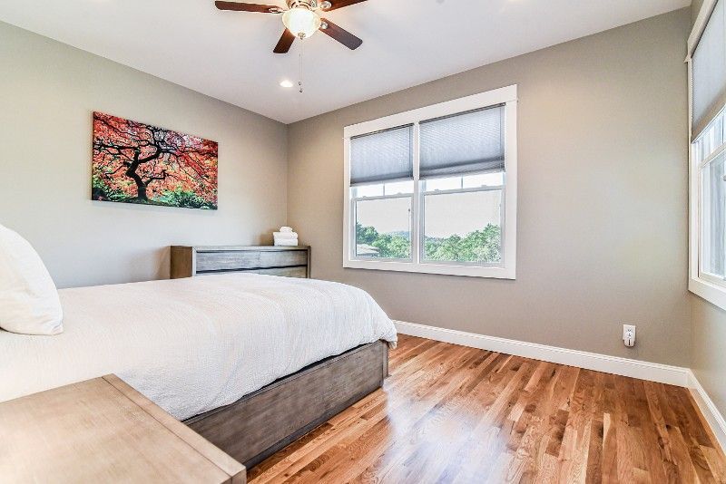 A bedroom with hardwood floors, a bed, two windows, and a ceiling fan.