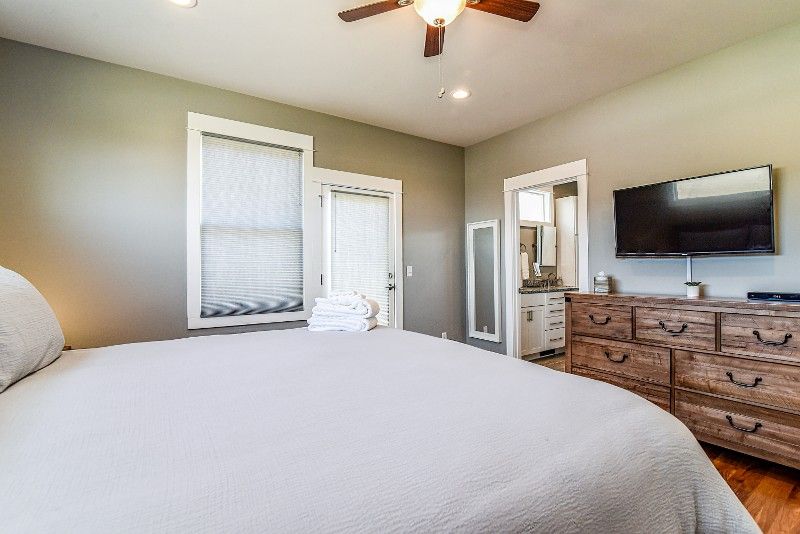 A bedroom with a king-size bed, dresser, television, and ceiling fan.
