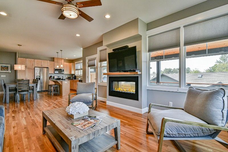 A living room with hardwood floors, a ceiling fan, a fireplace, and a flat-screen tv.