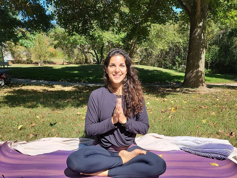 A woman is sitting on a yoga mat in a park.