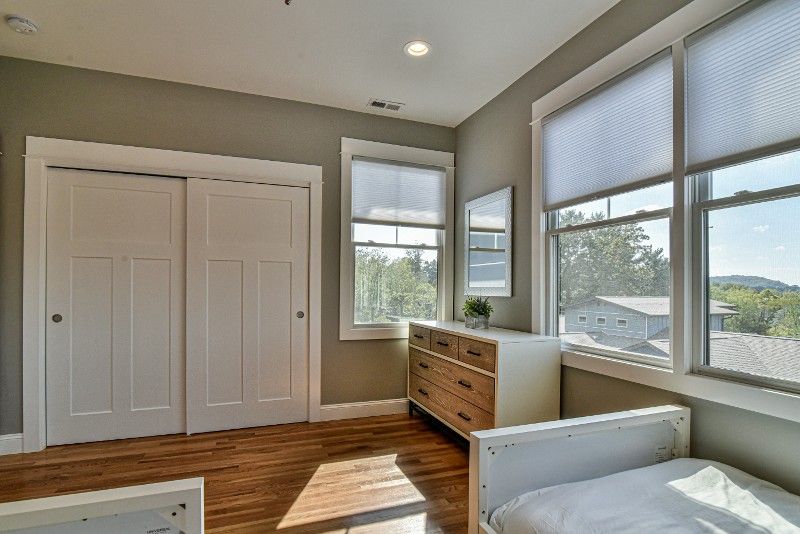 A bedroom with two beds, a dresser, and lots of windows.