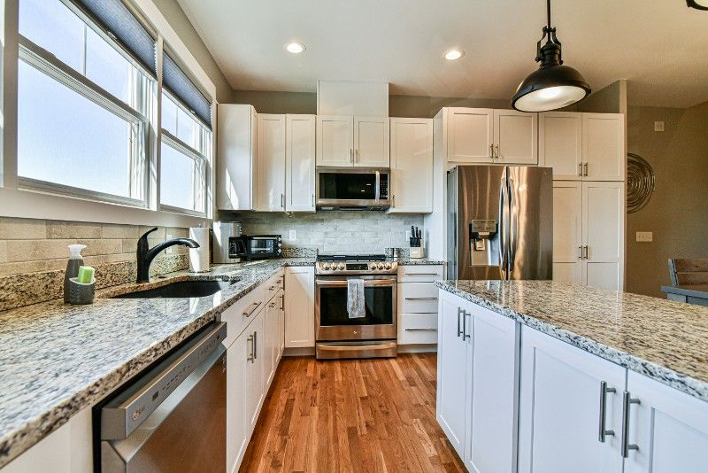 A kitchen with granite counter tops, stainless steel appliances, white cabinets, and hardwood floors.
