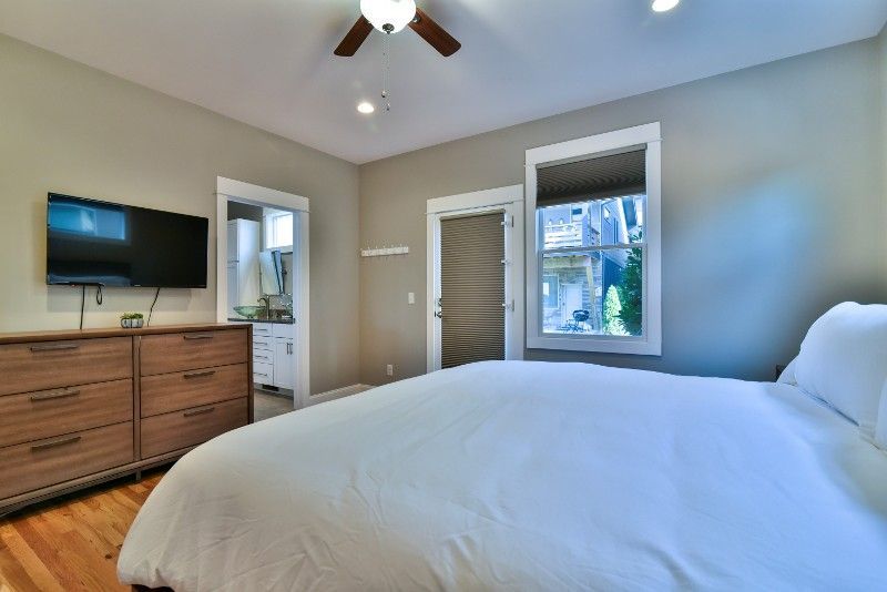 A bedroom with a bed, dresser, television, and a ceiling fan.