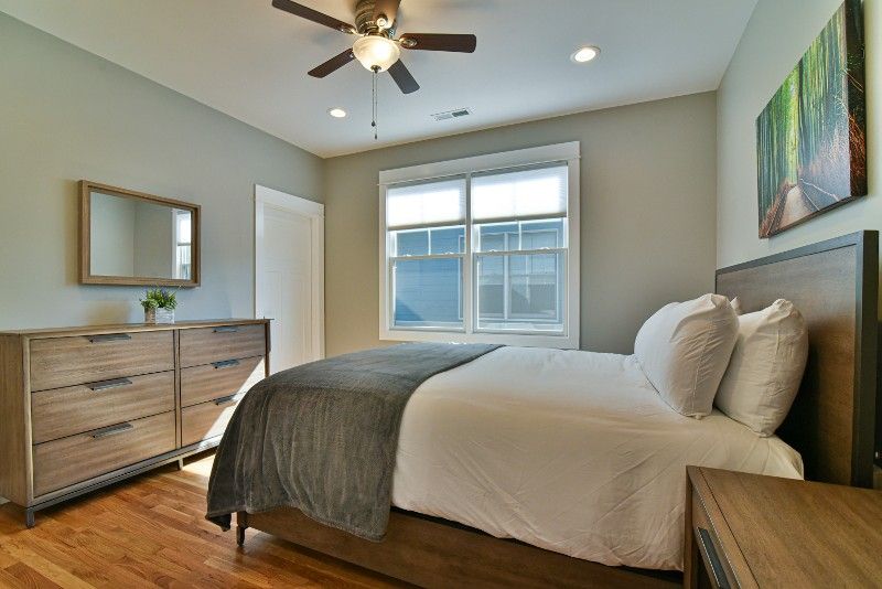 A bedroom with a bed, dresser, mirror, and ceiling fan.