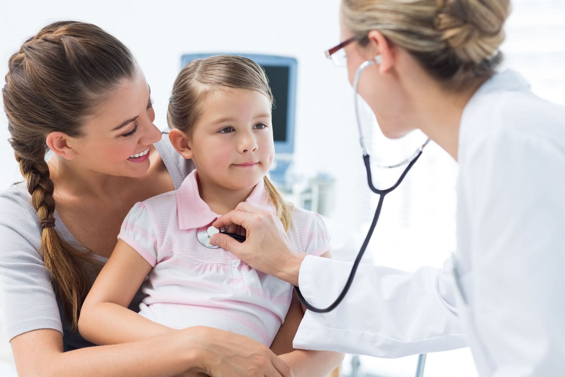 A doctor is listening to a little girl 's heart with a stethoscope.