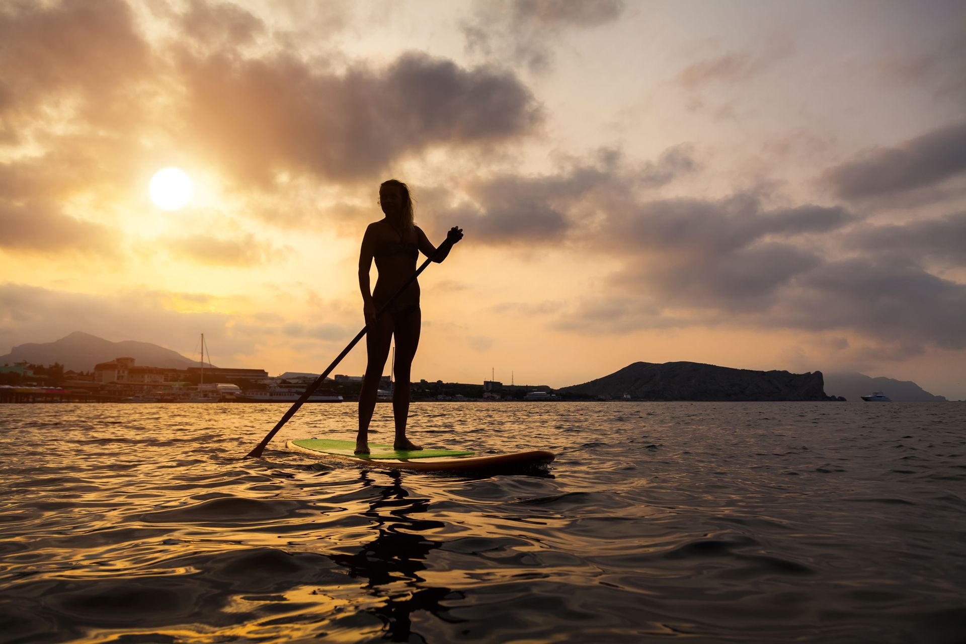 A woman is standing on a paddle board in the ocean at sunset.
