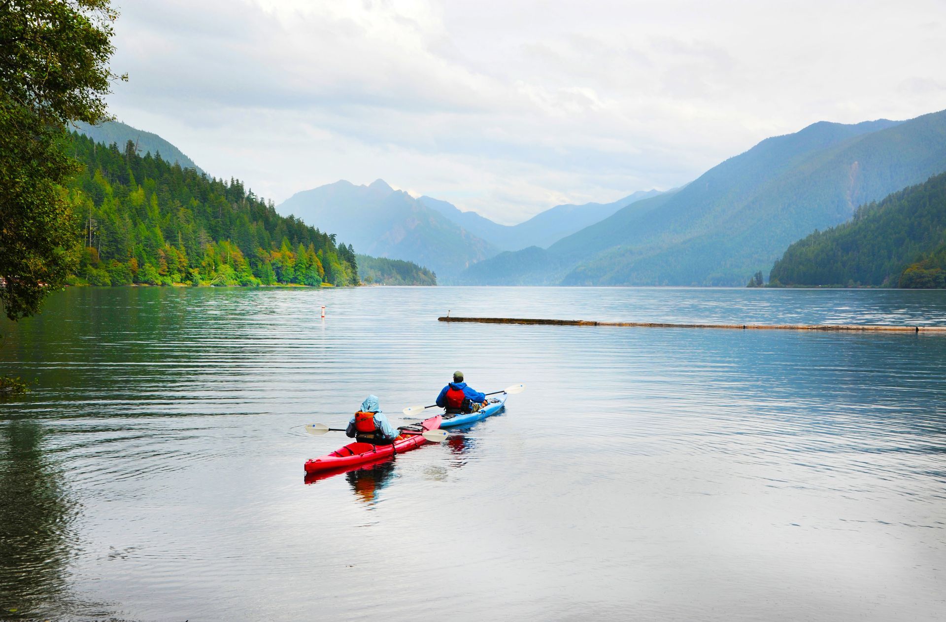 Two people are kayaking on a lake with mountains in the background.