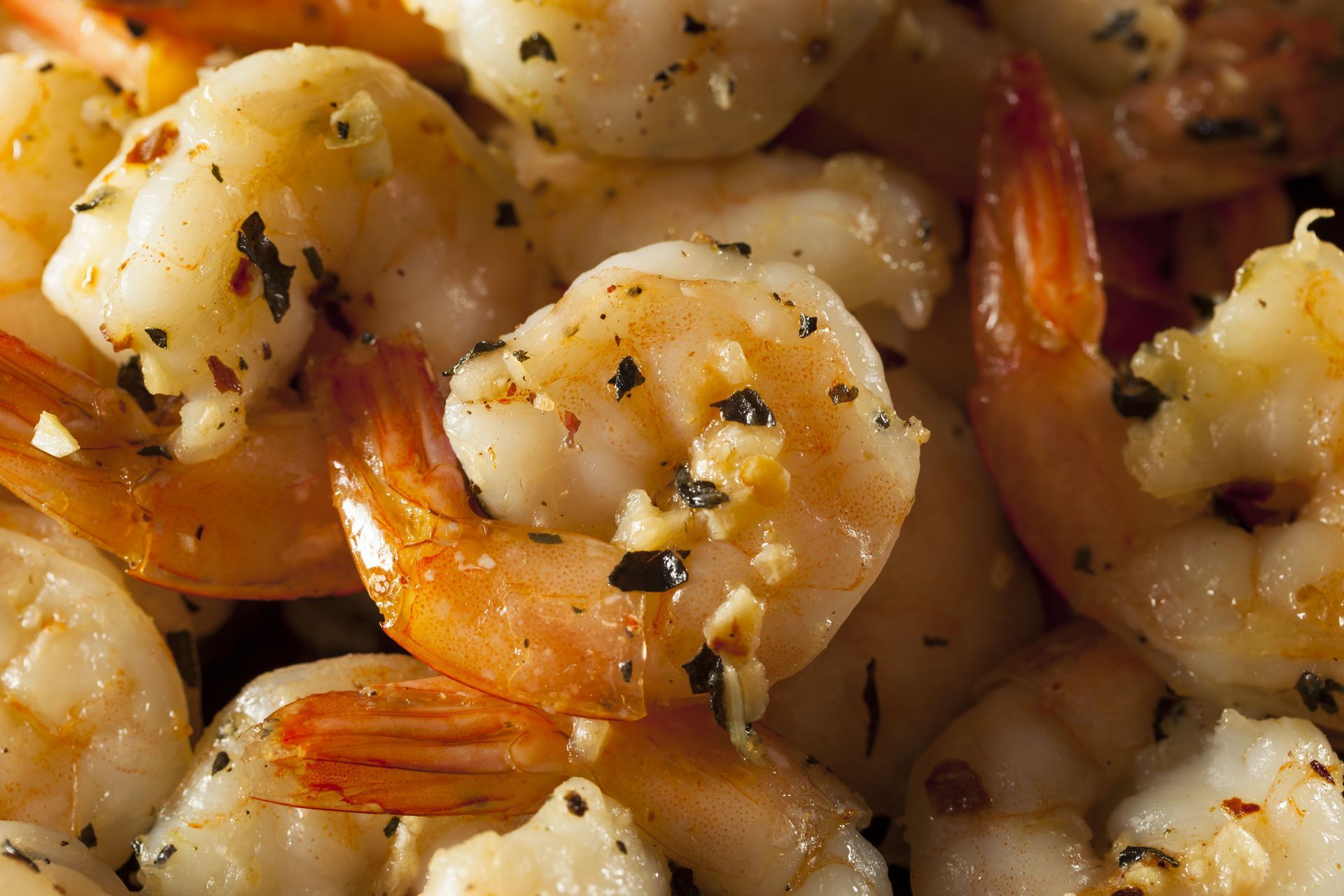 A close up of a pile of shrimp with garlic and herbs.