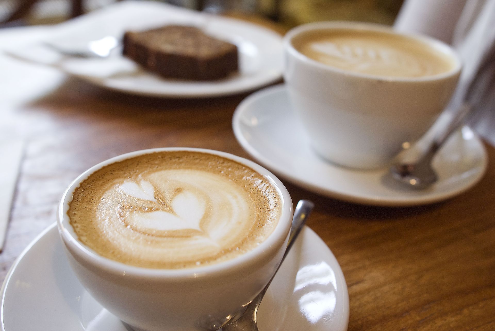 Two cups of cappuccino are on a saucer on a wooden table.