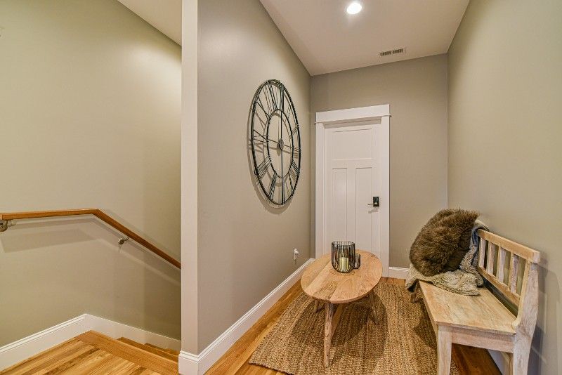 A hallway with stairs , a table , a bench and a clock on the wall.