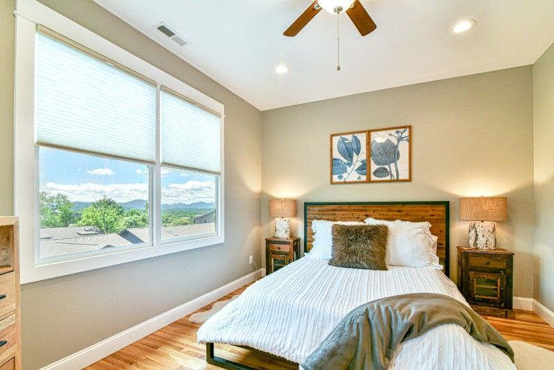 A bedroom with a bed, two nightstands, two windows, and a ceiling fan.