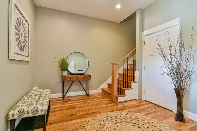 A hallway with hardwood floors, a bench, a mirror, and stairs.