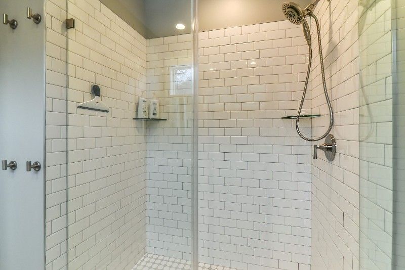 A bathroom with white brick walls and a walk in shower with a glass door.
