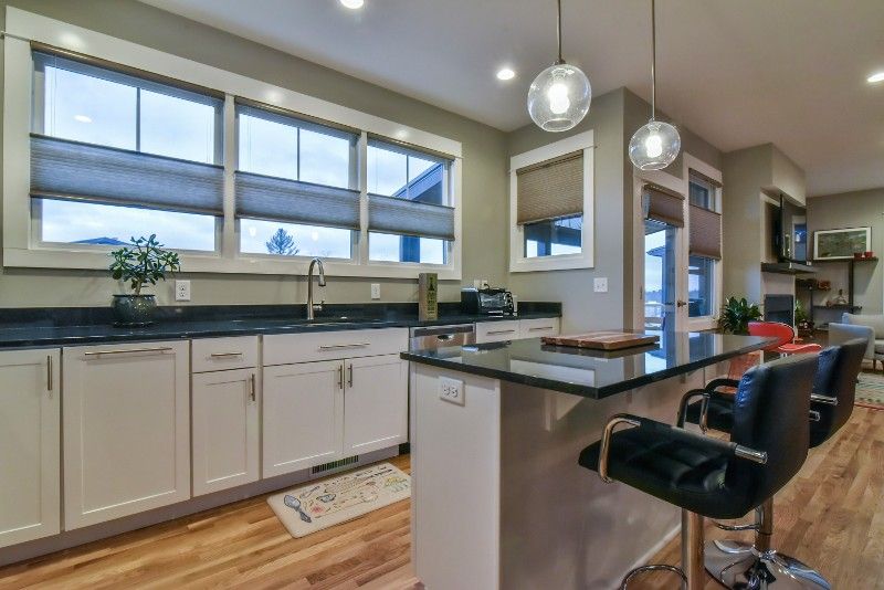A kitchen with white cabinets , black counter tops , and a bar.