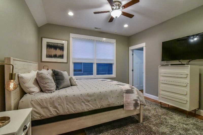 A bedroom with a bed , dresser , television and ceiling fan.