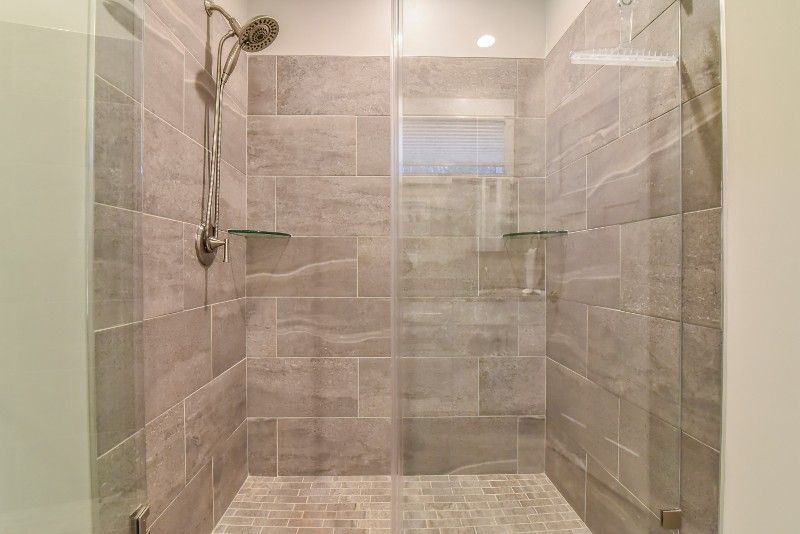 A walk in shower with a glass door and tiled walls.
