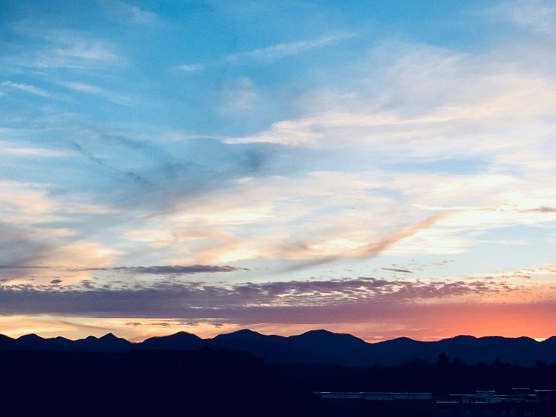 A sunset over a mountain range with a blue sky and clouds.
