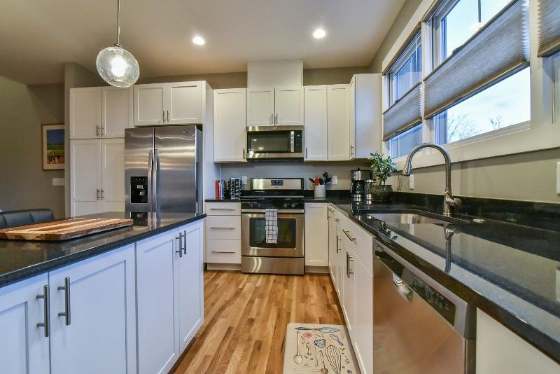 A kitchen with white cabinets, stainless steel appliances, granite counter tops, and hardwood floors.