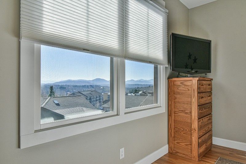 A bedroom with two windows , a dresser and a flat screen tv.