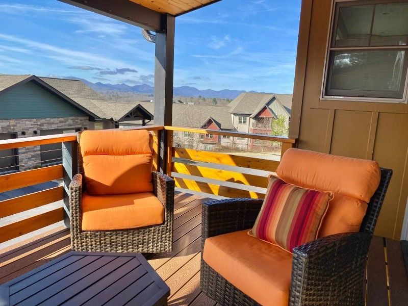 A balcony with two chairs and a table with mountains in the background