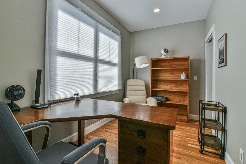 A home office with a desk , chair , bookshelf and window.