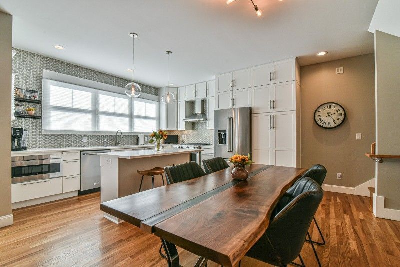 A dining room table and chairs in a kitchen with a clock on the wall.