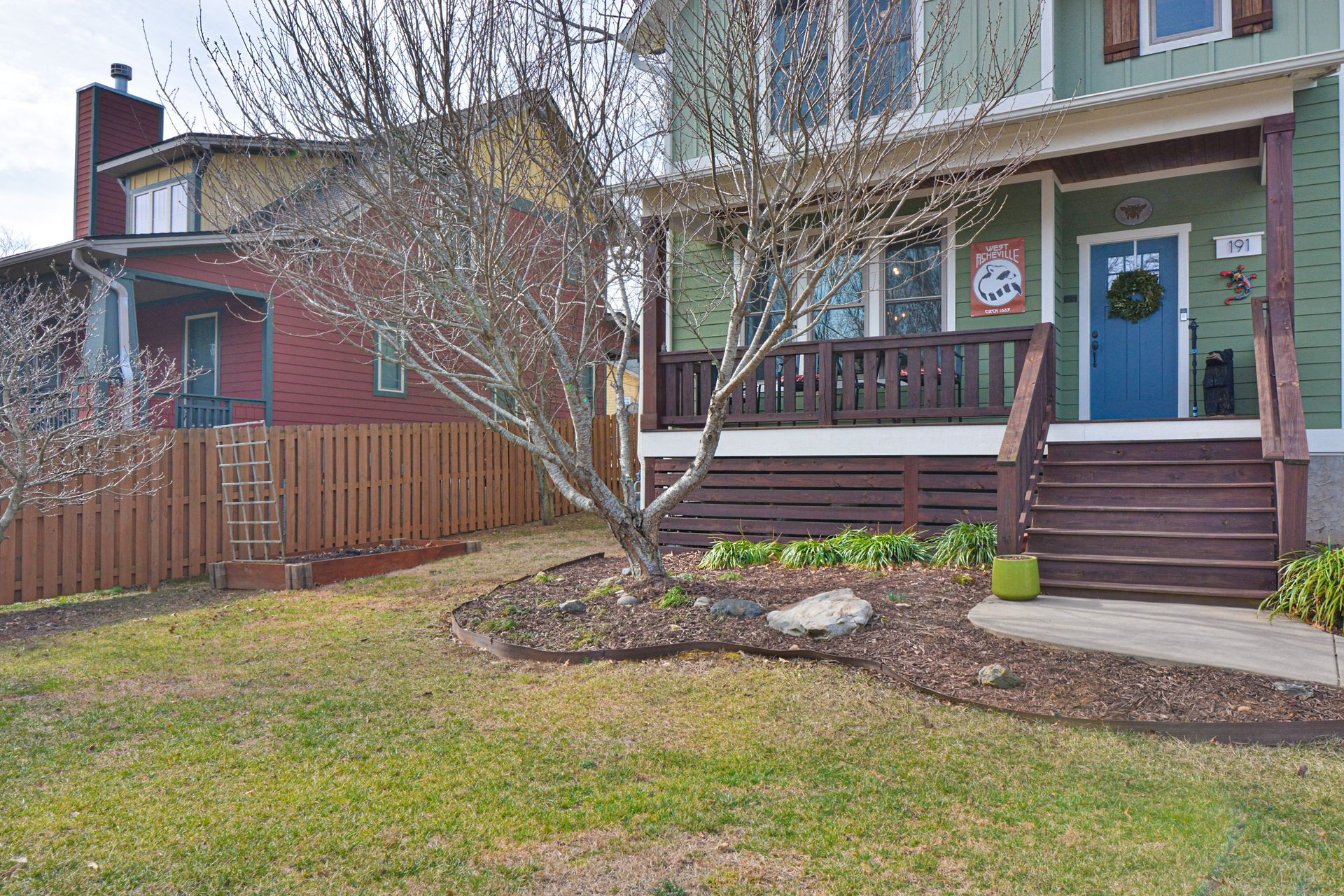 A green house with a blue door and front porch sits next to a red house with a brown fence on a sunny day.