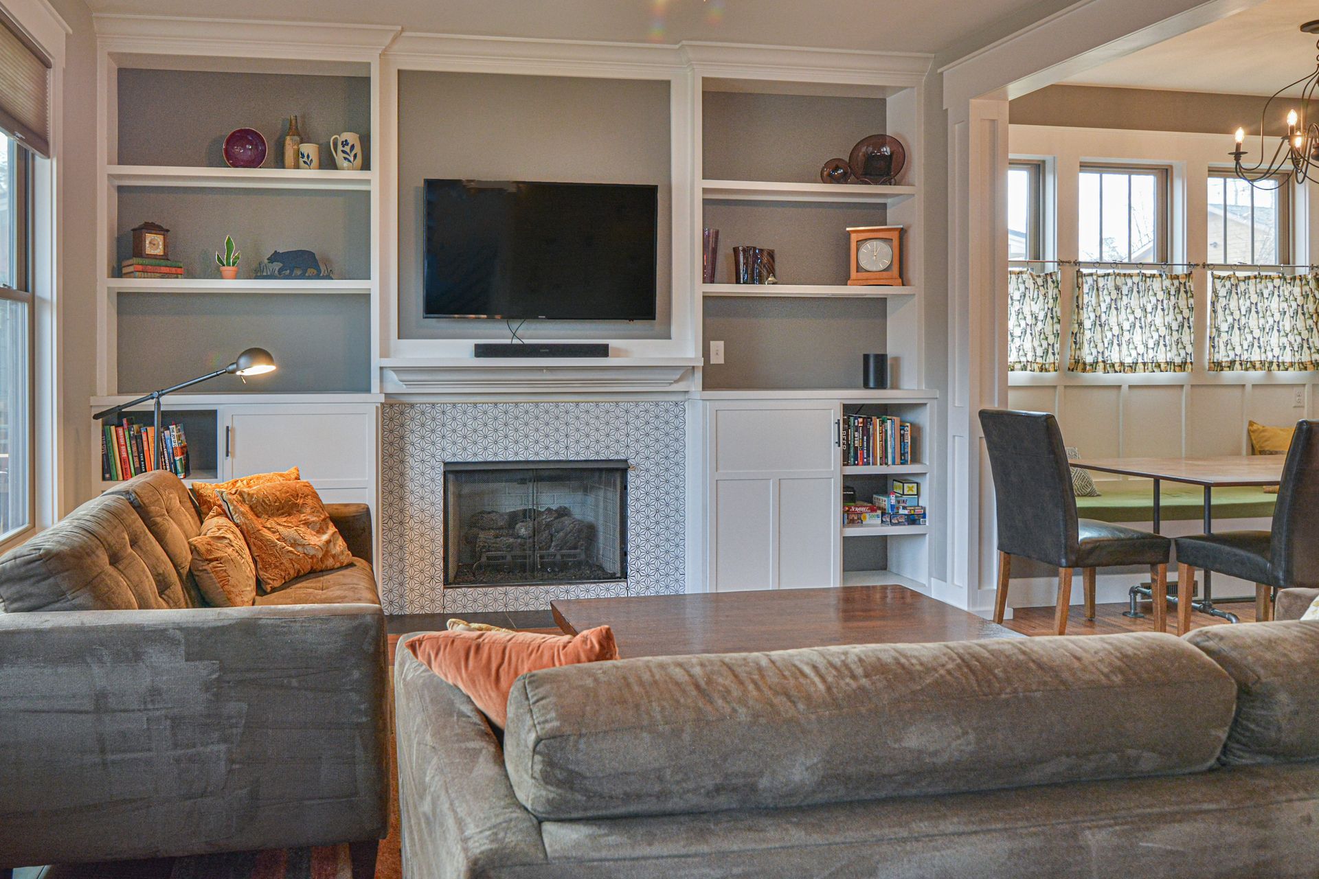 Living room with a gray sofa, a fireplace featuring patterned tile, and built-in shelving, leading to a dining area.