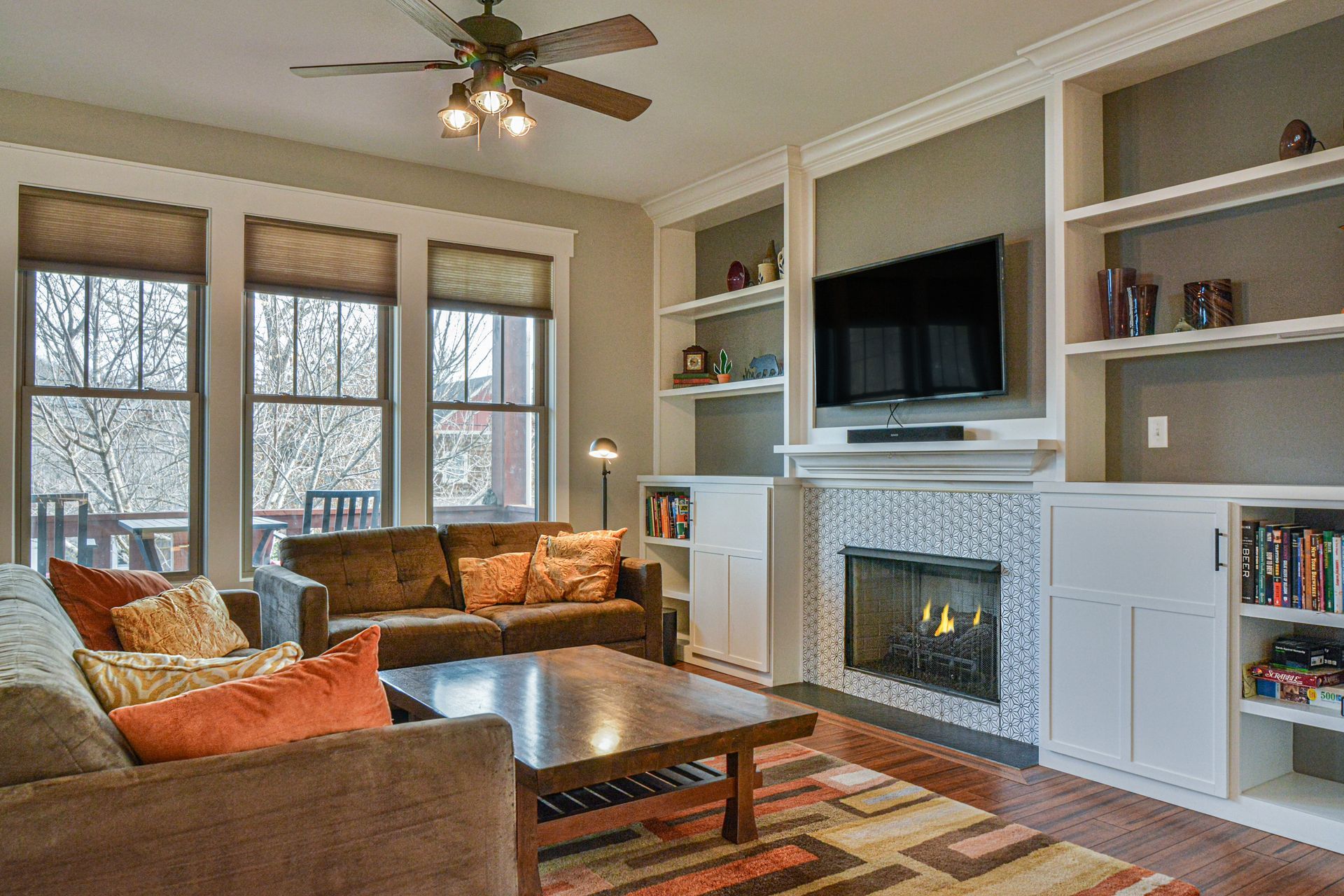 A cozy living room with a brown sofa, wooden coffee table, fireplace, and built-in white shelving surrounding a TV.