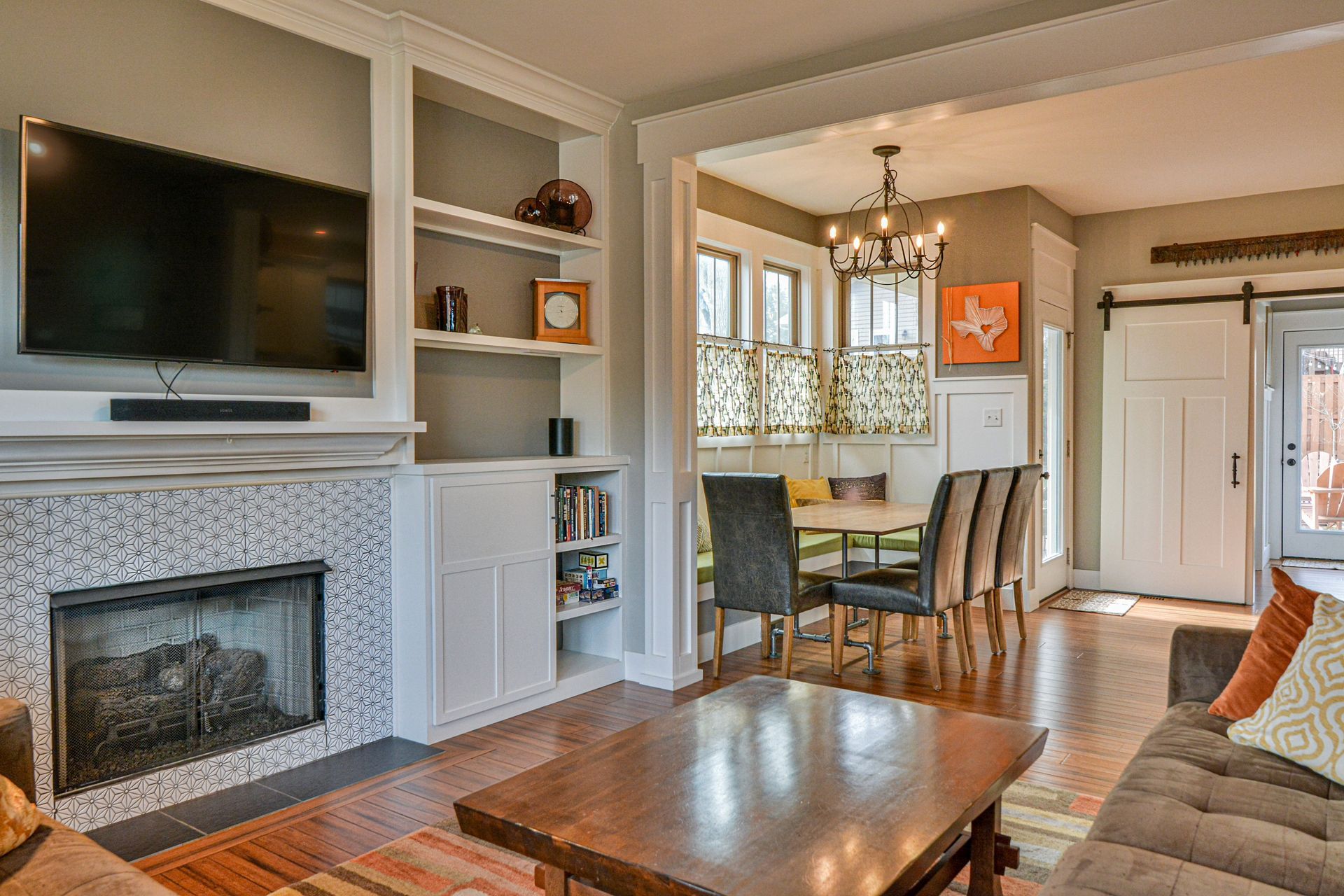 A living room with a fireplace, wall-mounted TV, built-in shelves, and a dining area with a table and chairs.