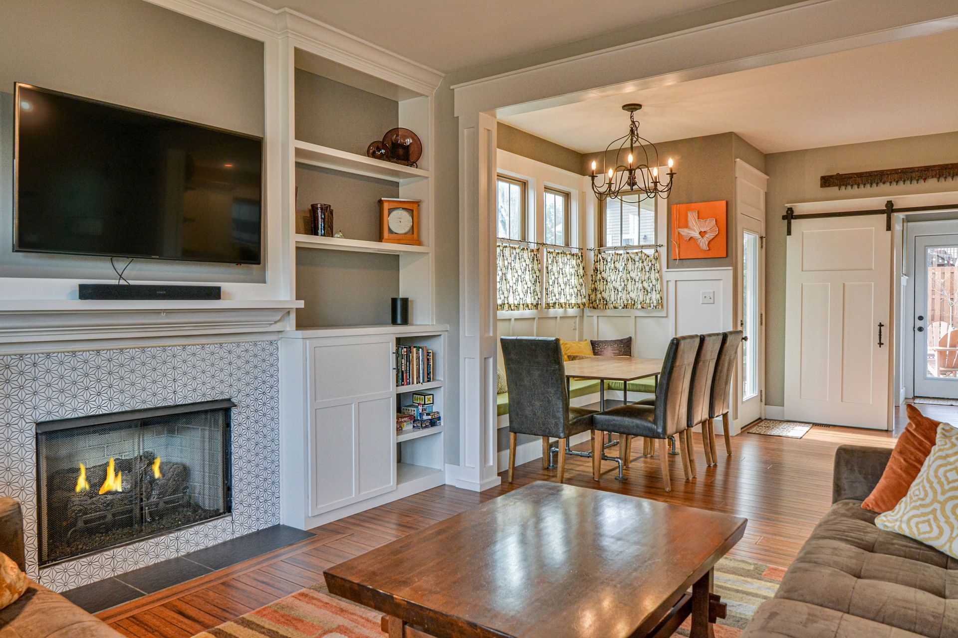 A living room with a fireplace, wall-mounted TV, built-in shelves, and a dining area visible through an open doorway.