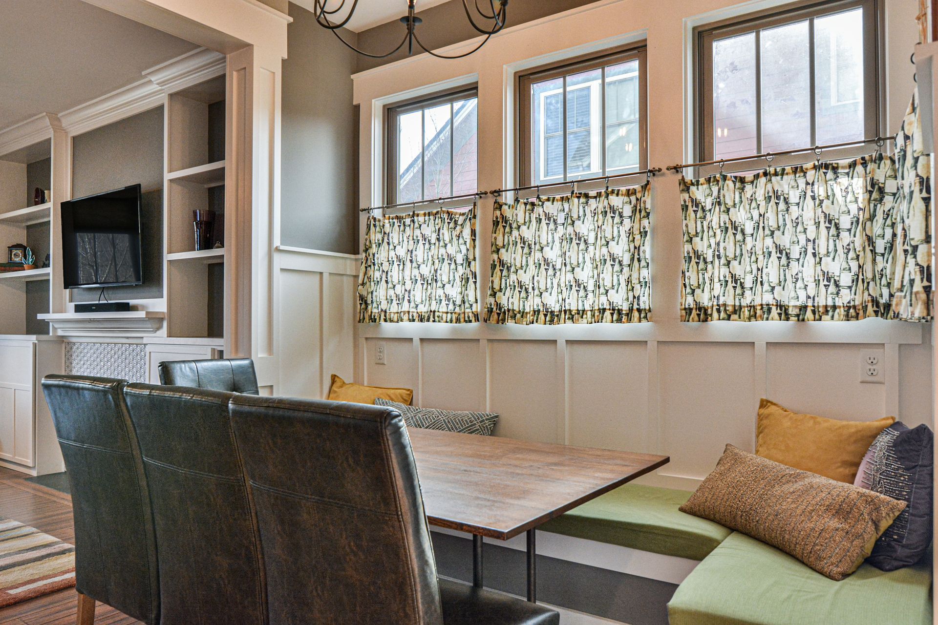 Dining area with a wooden table, dark leather chairs, and L-shaped bench seating with green cushions and accent pillows.
