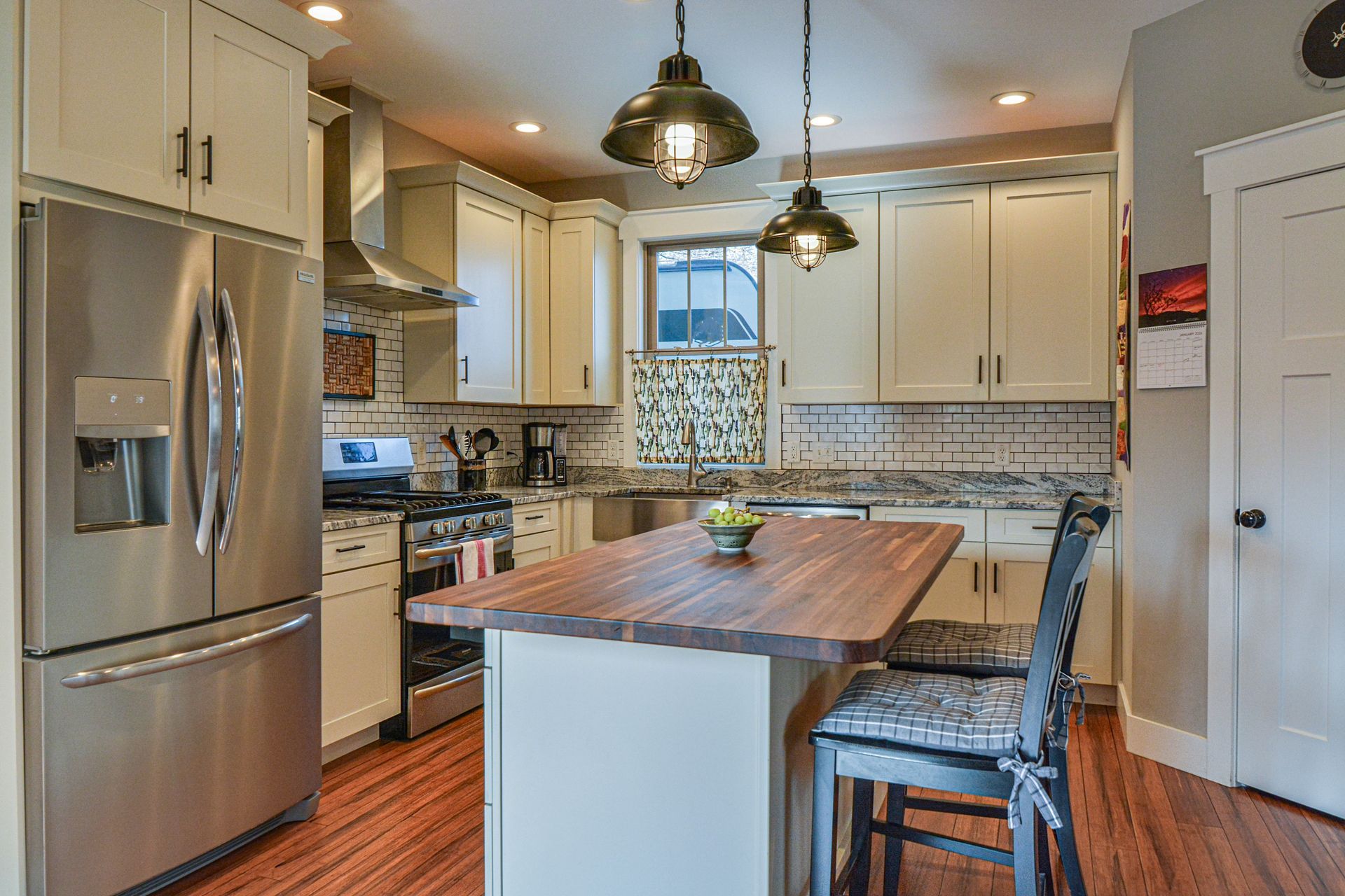 Modern kitchen with cream cabinets, stainless steel appliances, a wood-topped island, and two stools under pendant lights.