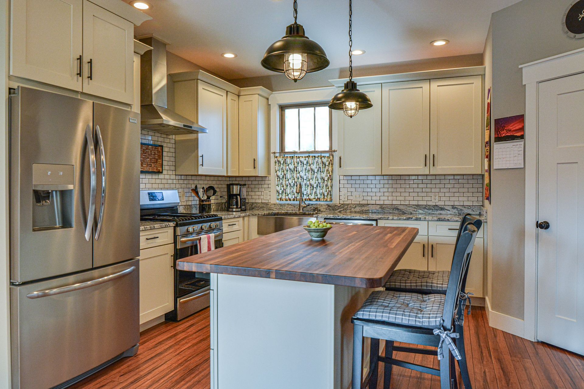 A kitchen with white cabinets, a wooden-topped island, stainless steel appliances, and two chairs on a hardwood floor.