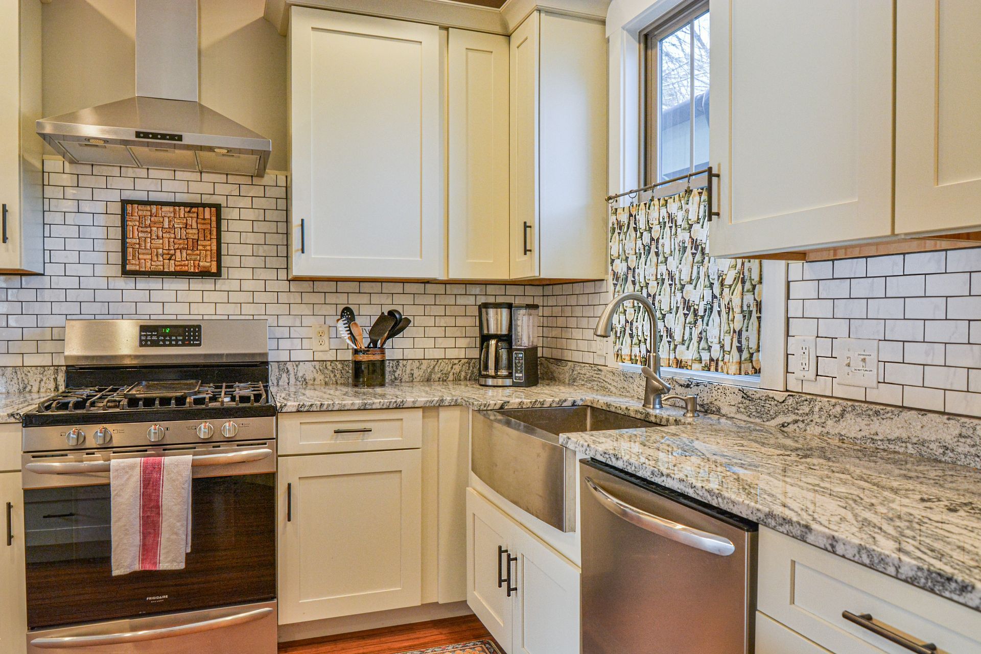 A modern kitchen with cream cabinets, white subway tile backsplash, granite countertops, and stainless steel appliances.