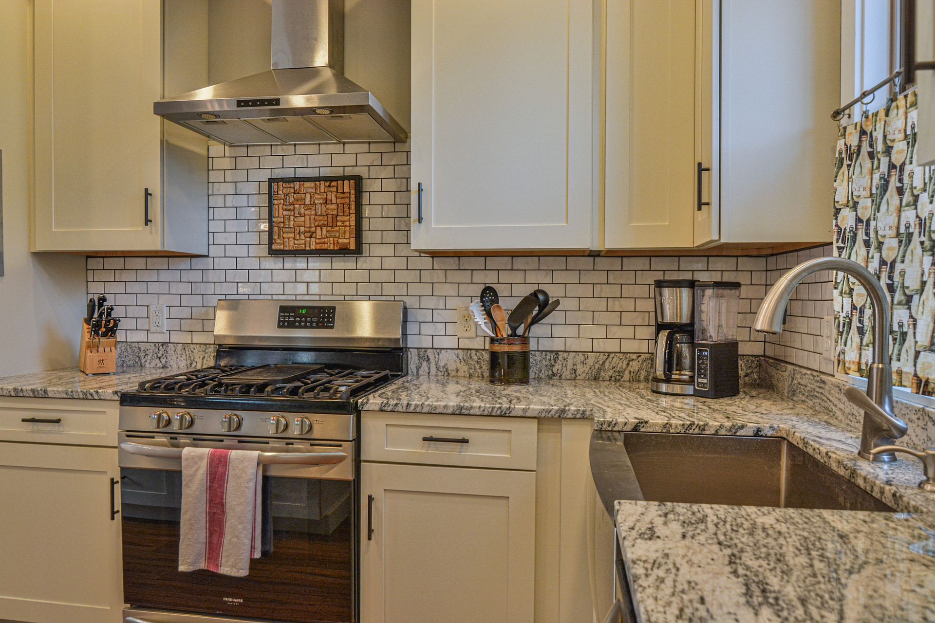 A modern kitchen features white cabinetry, granite countertops, a stainless steel gas range, and subway tile backsplash.