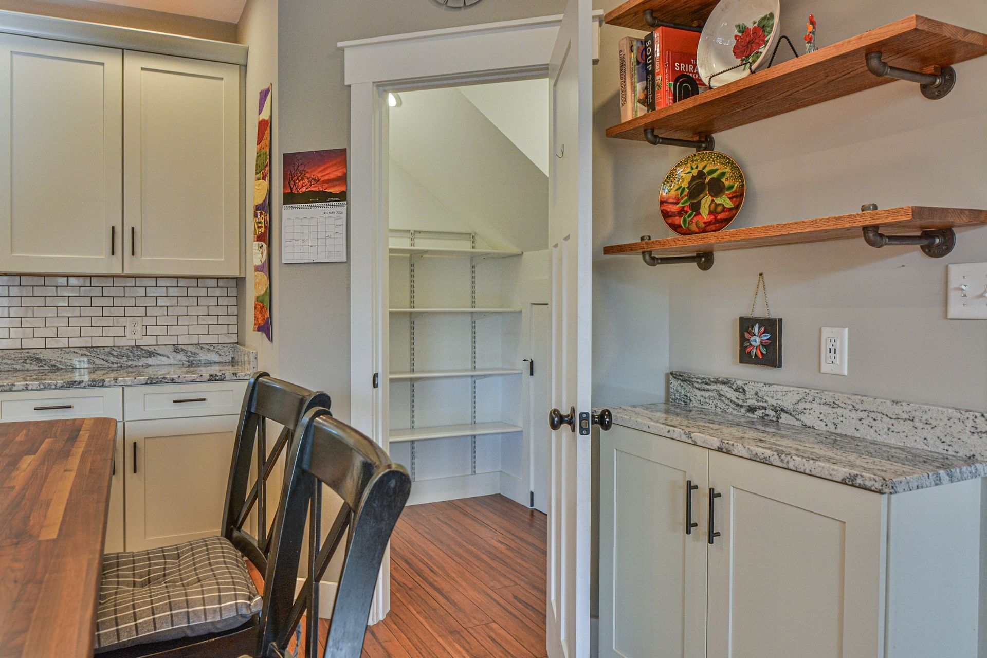 A pantry doorway between two sets of kitchen cabinets with white countertops, gray walls, and open wooden wall shelves.