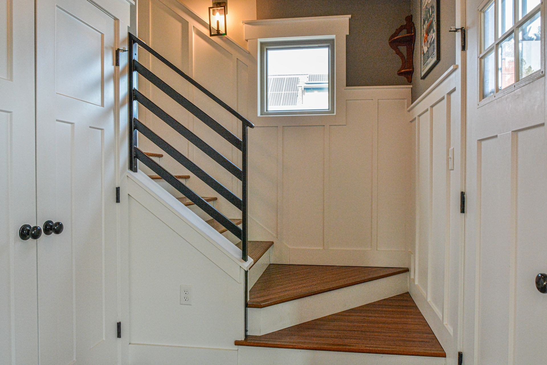 A staircase with wood steps, white board-and-batten walls, and a black horizontal metal railing.