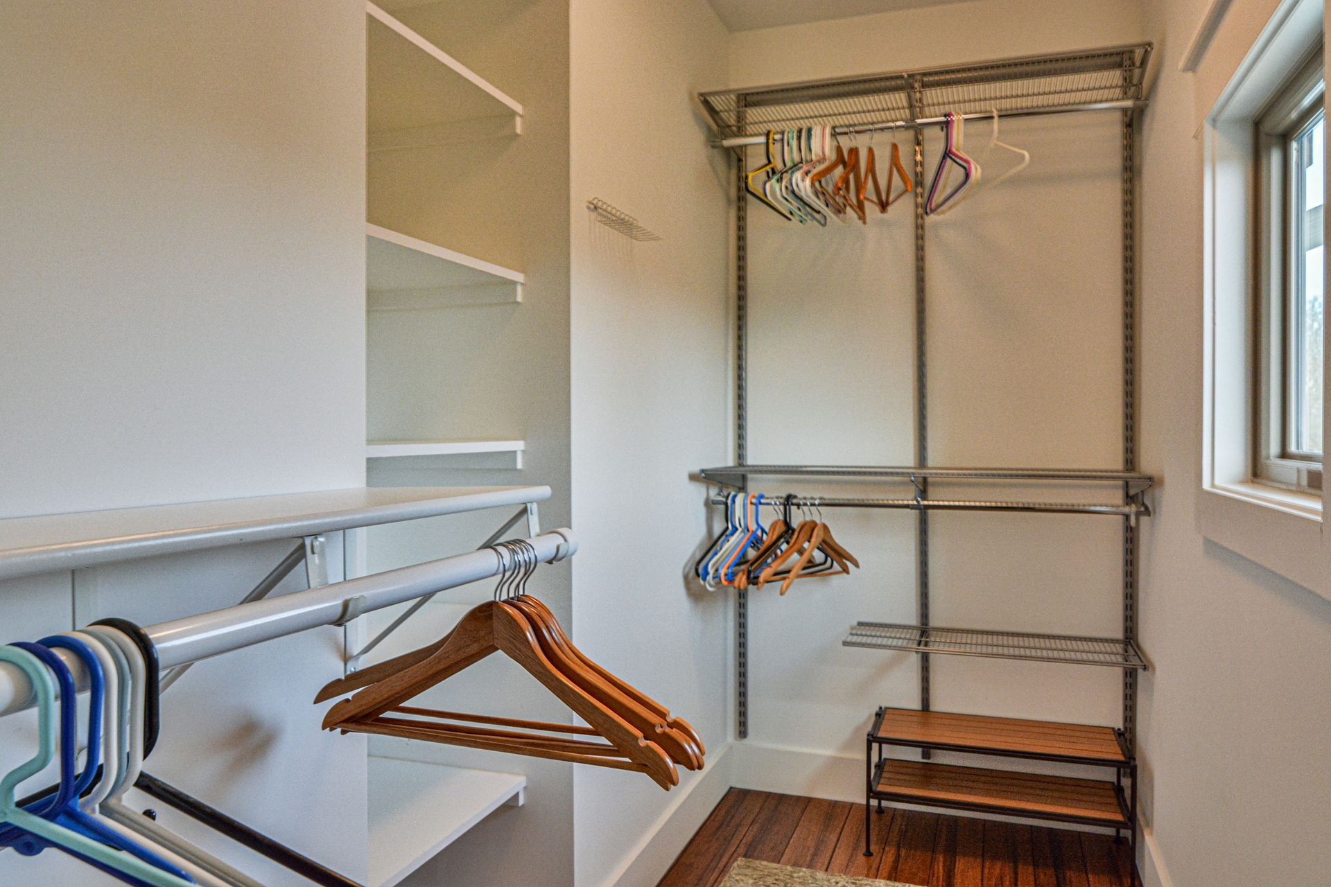 A walk-in closet featuring wire shelving, hanging rods with hangers, a small shoe rack, and a side window.
