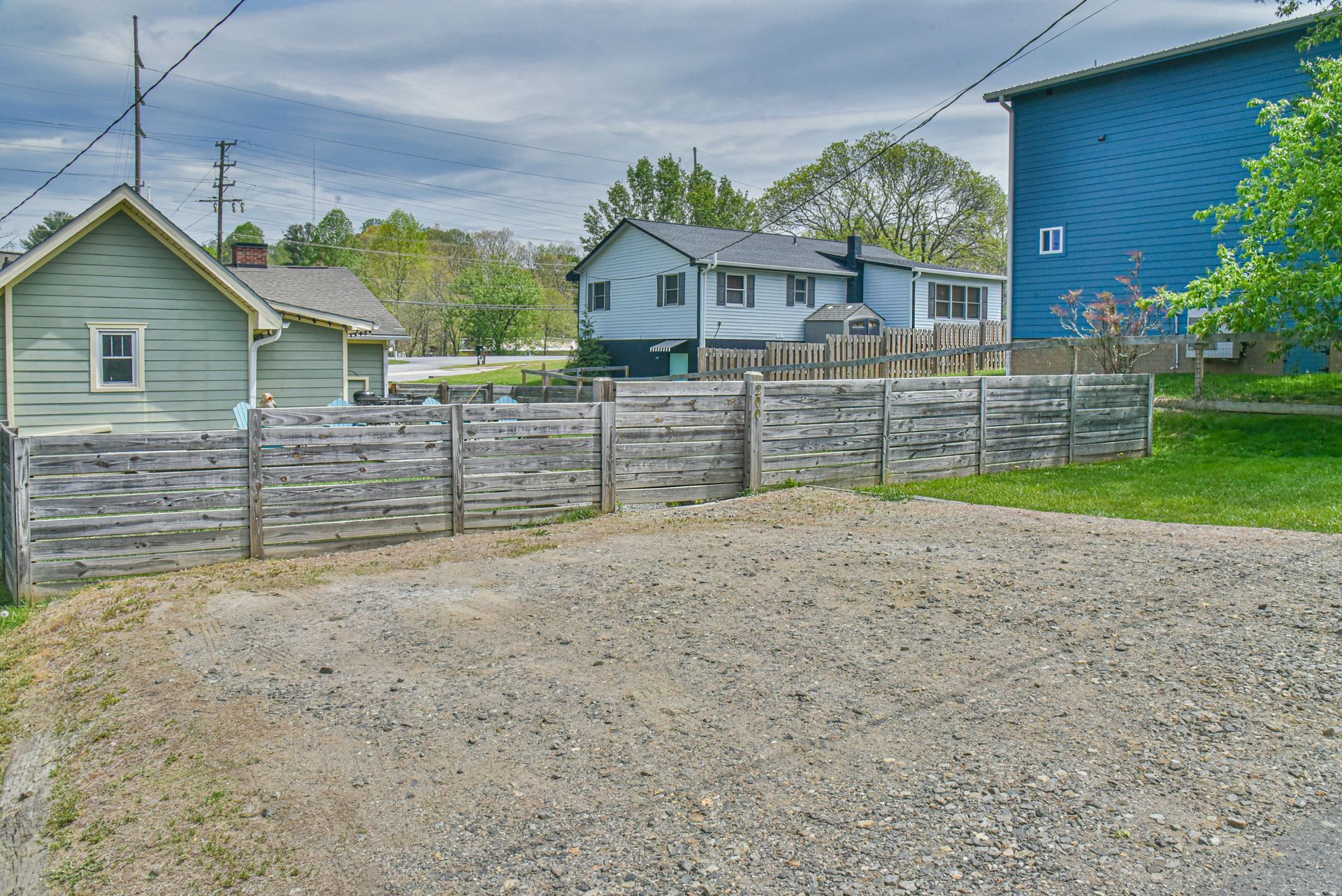 Gravel lot beside weathered wooden fence, with small houses and a blue building in the background.