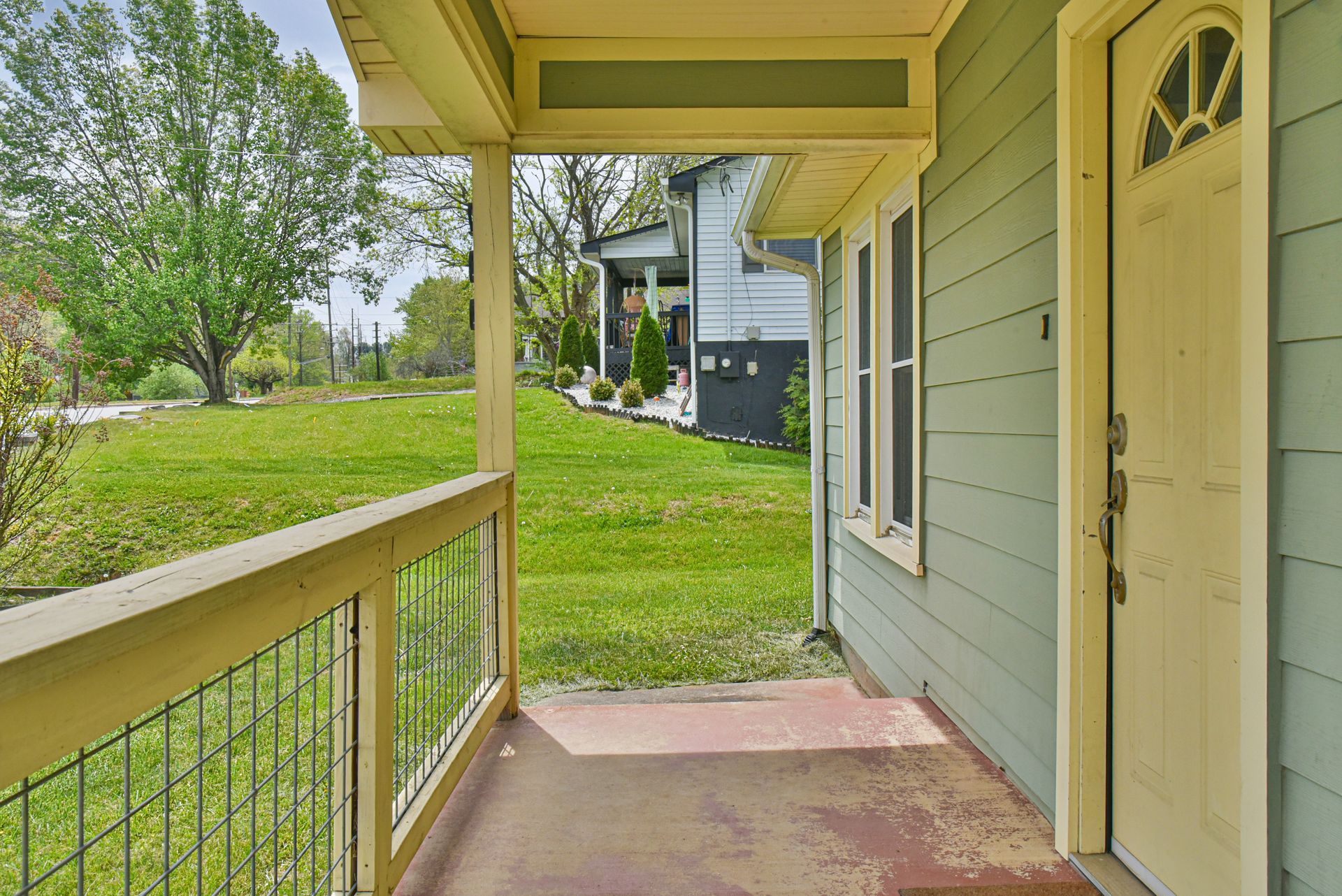 Covered apartment porch with green lawn and neighboring building in view