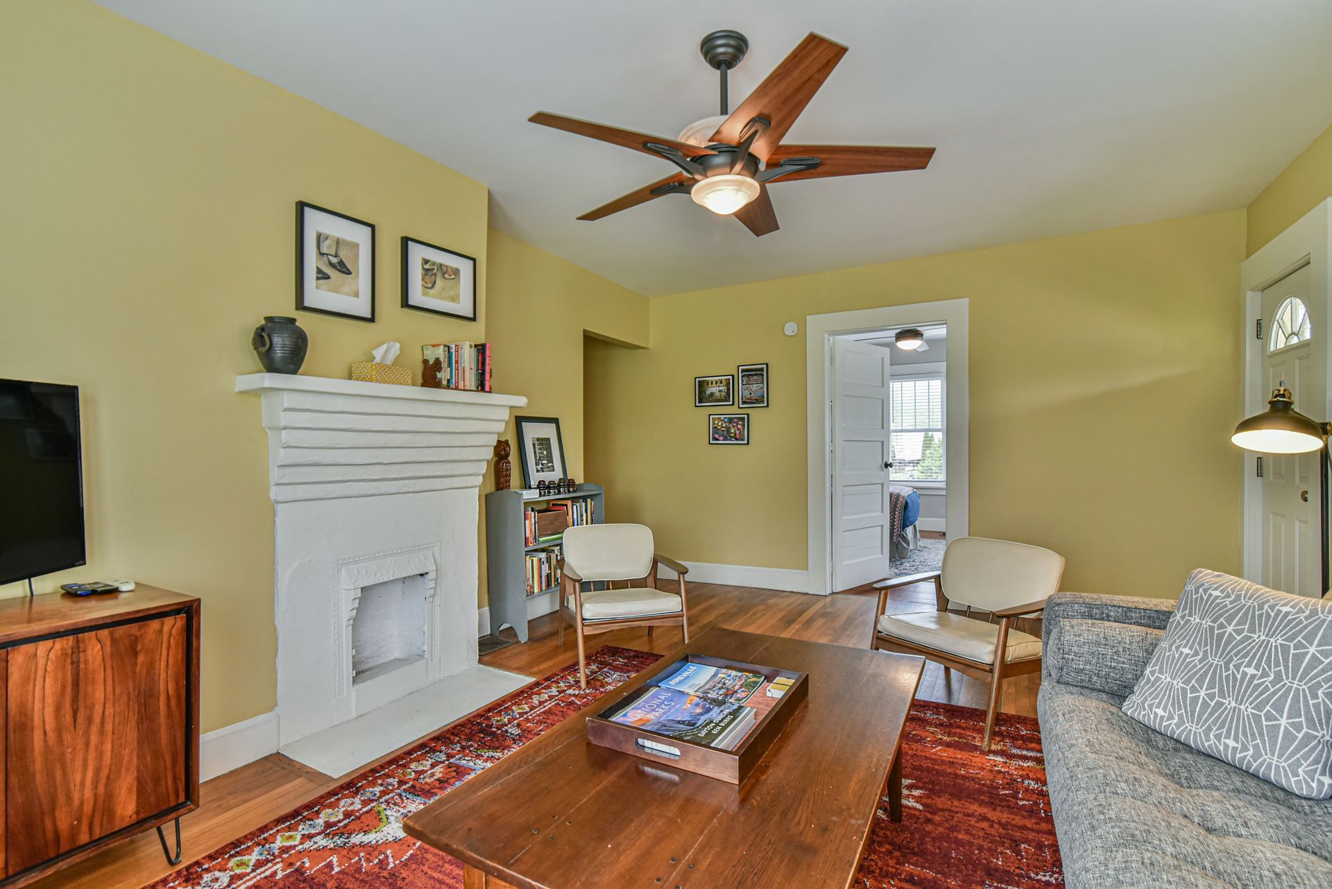 Living room with white fireplace, wood coffee table, patterned rug, and ceiling fan