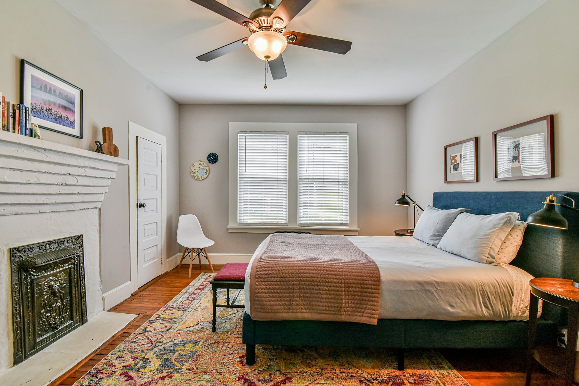 Cozy bedroom with a bed, fireplace, patterned rug, ceiling fan, and window shutters